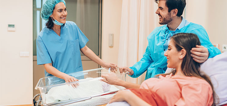 midwife at newborns bassinet with new parents in hospital room