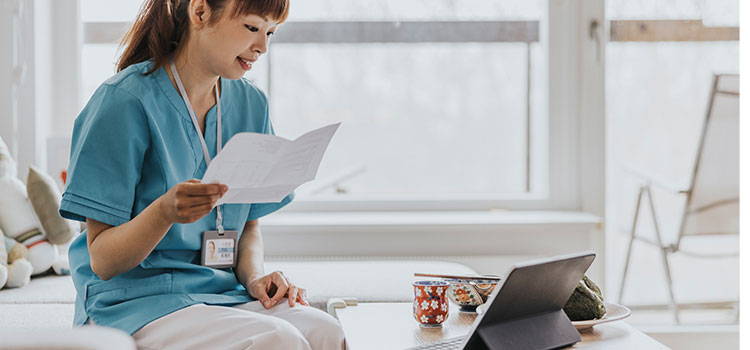 dermatology nurse holding paperwork and looking at laptop computer