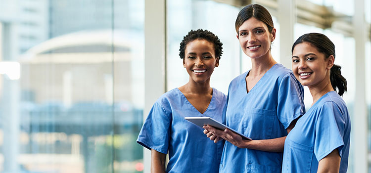 three smiling people in scrubs standing in healthcare foyer