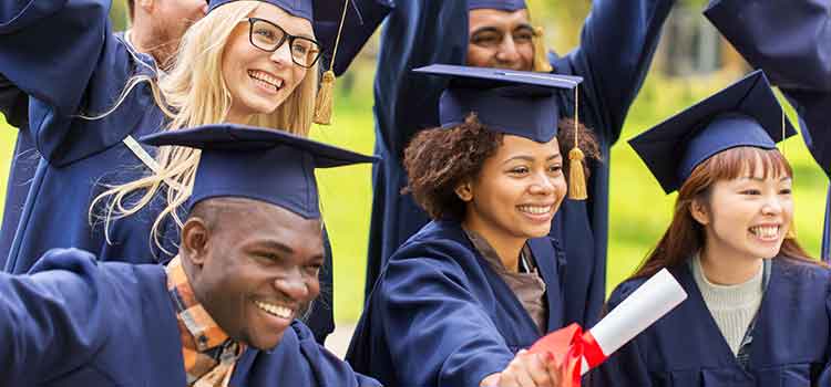several college graduates in caps and gowns cheering with diplomas