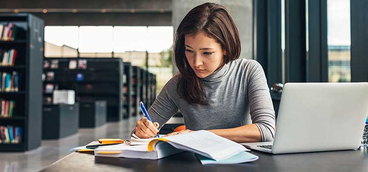 woman researching programs and writing in notebook