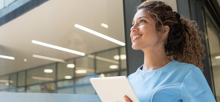professional in scrubs holding tablet looks out window