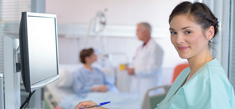 nurse standing in front of patient vitals on computer screen