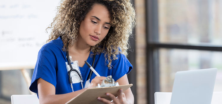 nurse taking notes while doing research online