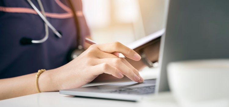 close-up of nurse with stethoscope typing on her laptop