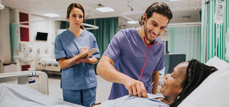 male nurse listens to heart of patient while teacher looks on