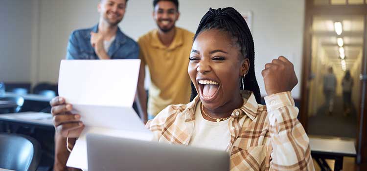 woman sits in front of laptop and cheers at the letter she is reading