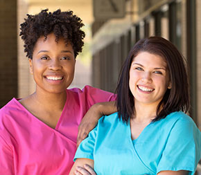 two female nurses in scrubs smile at the camera