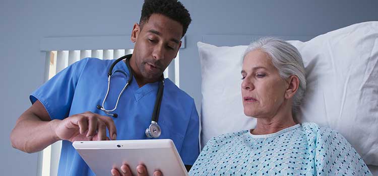 male nurse practitioner explains procedure to elderly woman lying in hospital bed