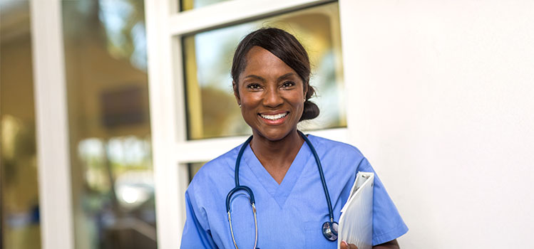 a middle-aged female nurse stands outside of a healthcare building