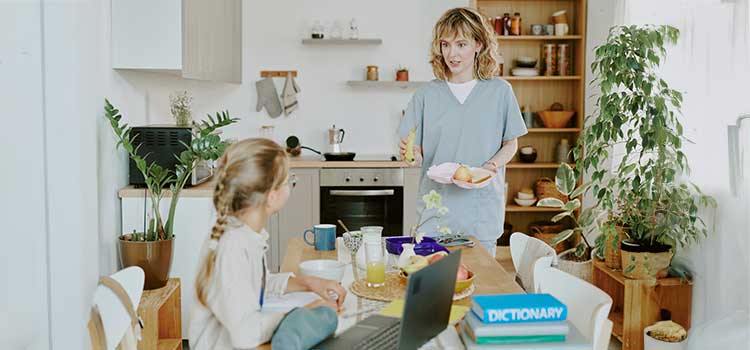 nursing student and parent brings sandwich to young daughter at dining room table