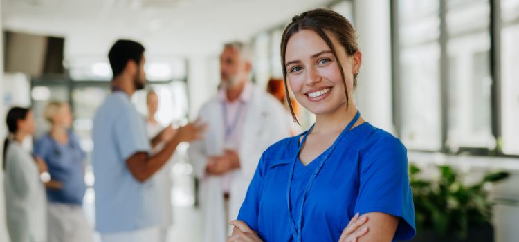 a nurse stands with her arms crossed and smiles at the camera